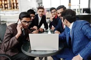 groupe de six hommes d'affaires indiens en costumes assis au bureau sur un café et regardant un ordinateur portable. photo