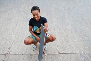 jeune femme afro-américaine posée avec planche à roulettes dans le skate park. photo