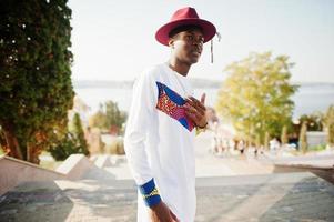 homme afro france élégant et branché en chapeau rouge et tenue blanche posée au jour de l'automne. gars modèle africain noir. photo