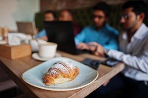 croissant sur fond de froup de quatre hommes sud-asiatiques posés lors d'une réunion d'affaires au café. photo