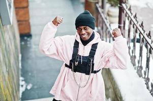 un homme afro-américain élégant de style urbain en sweat à capuche rose posé le jour de l'hiver montre les muscles des mains. photo