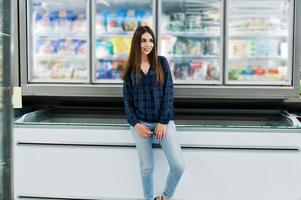 femme commerçante regardant les étagères du supermarché. portrait d'une jeune fille dans un magasin de marché prenant des fruits de mer du réfrigérateur. photo