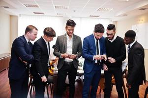 six hommes d'affaires multiraciaux debout au bureau et utilisant des téléphones portables. groupe diversifié d'employés masculins en tenue de soirée avec téléphones portables. photo