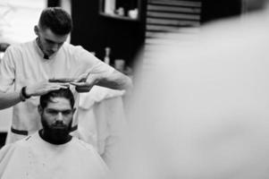 jeune homme barbu se coupe les cheveux par un coiffeur assis sur une chaise au salon de coiffure. âme de barbier. photo