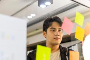 homme d'affaires pensant écrivant sur des notes colorées attachées à un mur de verre l'entrepreneur crée une liste visuelle de planification. photo