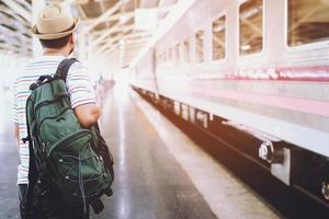 les passagers attendent le quai de la gare. jeune homme voyageur avec sac à dos à la recherche d'un train en attente. le voyage touristique se prépare pour le concept de départ. photo