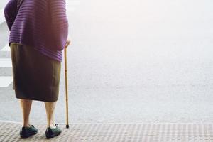 vieille femme âgée avec bâton de marche attendant sur le trottoir du sentier traversant la rue seule. concept senior de l'autre côté de la rue jusqu'au passage pour piétons zèbre. photo