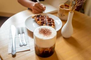 un repas du dimanche matin au café, deux tasses de café, un latte au miel et un eispanner americano servis avec une gaufre sur une assiette, décorés d'un vase. photo