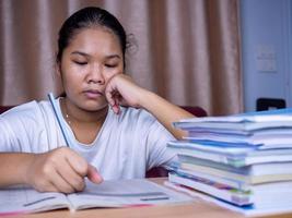 fille faisant ses devoirs sur une table en bois et il y avait une pile de livres à côté le fond est un canapé rouge et des rideaux crème. photo