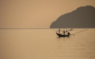 un petit bateau de pêche amarré au milieu de la mer au coucher du soleil.