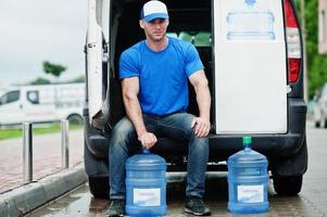 livreur devant une camionnette livrant des bouteilles d'eau. photo