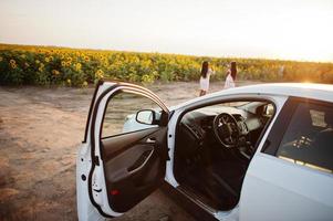 voiture blanche contre deux jolies femmes noires portent une robe d'été pose dans un champ de tournesol. photo