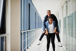 deux amies africaines en veste de jeans s'amusant, ont sauté sur les épaules ensemble à l'intérieur. photo