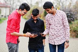 trois amis étudiants indiens marchant dans la rue et regardant un téléphone portable. photo