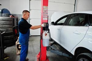 thème de la réparation et de l'entretien des voitures. mécanicien en uniforme travaillant en service automatique, appuyez sur le bouton pour soulever l'auto. photo