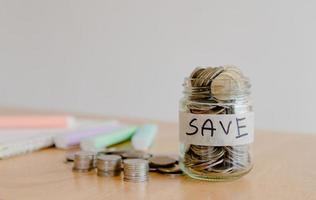 main de femme asiatique met une pièce de monnaie dans une bouteille en verre sur une table en bois, entreprise d'investissement, retraite, finances et économiser de l'argent pour un concept futur. photo