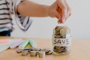 main de femme asiatique met une pièce de monnaie dans une bouteille en verre sur une table en bois, entreprise d'investissement, retraite, finances et économiser de l'argent pour un concept futur. photo