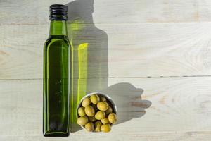huile d'olive extra vierge en bouteille verte et olives vertes fraîches sur table en bois.