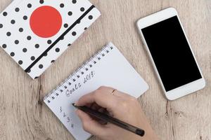 les mains de la jeune femme tiennent des pages de cahier ouvertes avec un stylo noir sur une table en bois. liste des objectifs 2019. photo