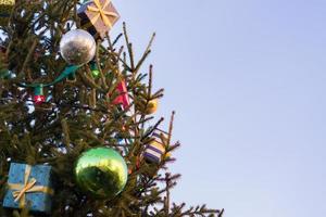 fond de vacances de noël et du nouvel an. arbre de noël décoré de boules, coffrets cadeaux et guirlandes contre le ciel bleu, espace copie photo