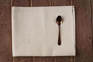 vue de dessus d'une serviette en tissu de couleur beige et d'une cuillère à thé servie sur une table en bois. photo