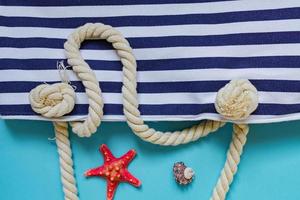 coquillages, étoiles de mer et sac bleu marine à rayures textiles avec nœuds de corde sur fond bleu clair. vacances d'été et concept de vacances photo