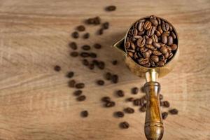 vue de dessus de grains de café torréfiés frais dans une cafetière turque traditionnelle cezve sur une table en bois. mise au point sélective photo