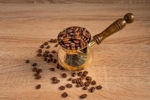 gros plan de grains de café torréfiés frais dans une cafetière turque traditionnelle cezve sur une table en bois. photo