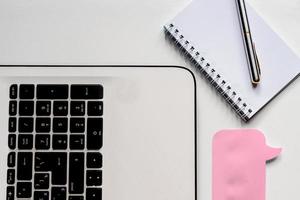 vue de dessus du bureau blanc, autocollant rose pour notes, ordinateur portable, stylo et carnet, maquette d'entreprise photo