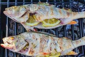 poisson de perche frais grillé avec des tranches de citron. cuisiner des fruits de mer barbecue sur le feu à l'extérieur. photo
