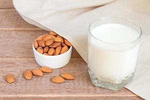 lait d'amande fait maison dans un verre et noix dans un bol en porcelaine blanche sur fond de bois photo