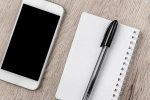 concept d'entreprise et de bureau - cahier vierge, smartphone et stylo noir sur table en bois. mise à plat minimale, vue de dessus. photo