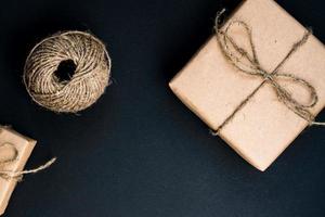 coffret cadeau artisanal enveloppé dans du papier kraft avec corde et arc sur fond noir. vue de dessus, mise à plat photo