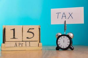 concept de rappel de jour d'impôt. Calendrier en bois du 15 avril et réveil avec bannière et phrase manuscrite sur table en bois. photo