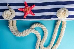 coquillages, étoiles de mer et sac bleu marine à rayures textiles avec nœuds de corde sur fond bleu clair. vacances d'été et concept de vacances