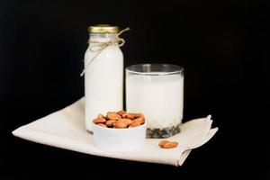 lait d'amande fait maison dans une bouteille et verre avec noix dans un bol en porcelaine blanche sur fond noir. se concentrer sur les noix photo