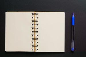 concept de design - vue de dessus d'un cahier kraft vide et d'un stylo à bille bleu sur fond noir. maquette. photo