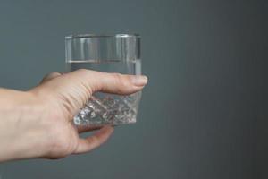 femme tenant un verre d'eau dans sa main sur fond gris photo