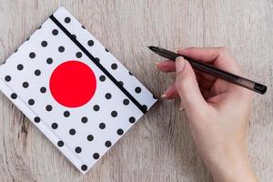 jeune femme main tenir un stylo noir et un cahier à couverture à pois sur une table en bois photo