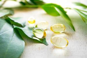 supplément de vitamines naturelles sur fond de bois blanc avec des feuilles vertes. photo