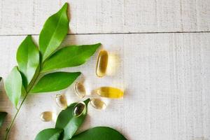 vue de dessus du supplément de vitamines naturelles sur fond de bois blanc avec des feuilles vertes. photo