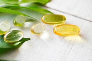 supplément de vitamines naturelles sur fond de bois blanc avec des feuilles vertes. photo