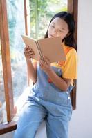 la fille tient le livre assis aux fenêtres en bois à la maison. photo