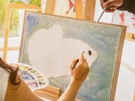 artiste de femmes asiatiques peignant le poisson dans la salle de classe pendant que son professeur enseigne et tuteur comment peindre, concept de poisson d'art photo