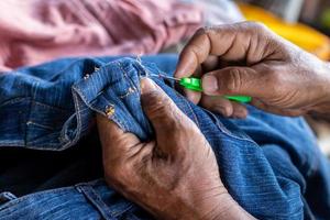 vue rapprochée des deux mains d'un homme thaïlandais âgé utilisant une aiguille pour ramasser des fils pour réparer les jeans. photo