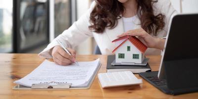 gros plan sur des mains de femme tenant un modèle de maison, des contrats de courtage immobilier à vendre et à louer avec des concepts de prêt hypothécaire d'assurance. photo