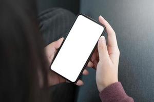 image de maquette téléphone portable à écran blanc vierge. main de femme tenant des SMS à l'aide d'un téléphone portable sur un canapé. photo