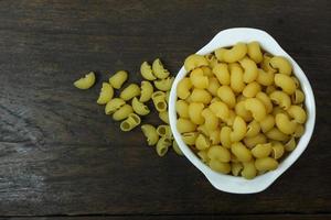 macaroni cru dans un bol blanc sur une table en bois photo