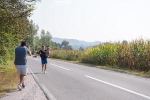 vidéaste enregistrant pendant qu'un couple fait du jogging le long d'une route de campagne photo