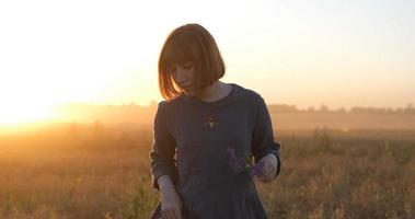 jeune femme rousse dans une belle robe bohème se relaxant sur le terrain pendant le coucher du soleil brumeux, femme à l'extérieur avec bouquet dans les mains photo